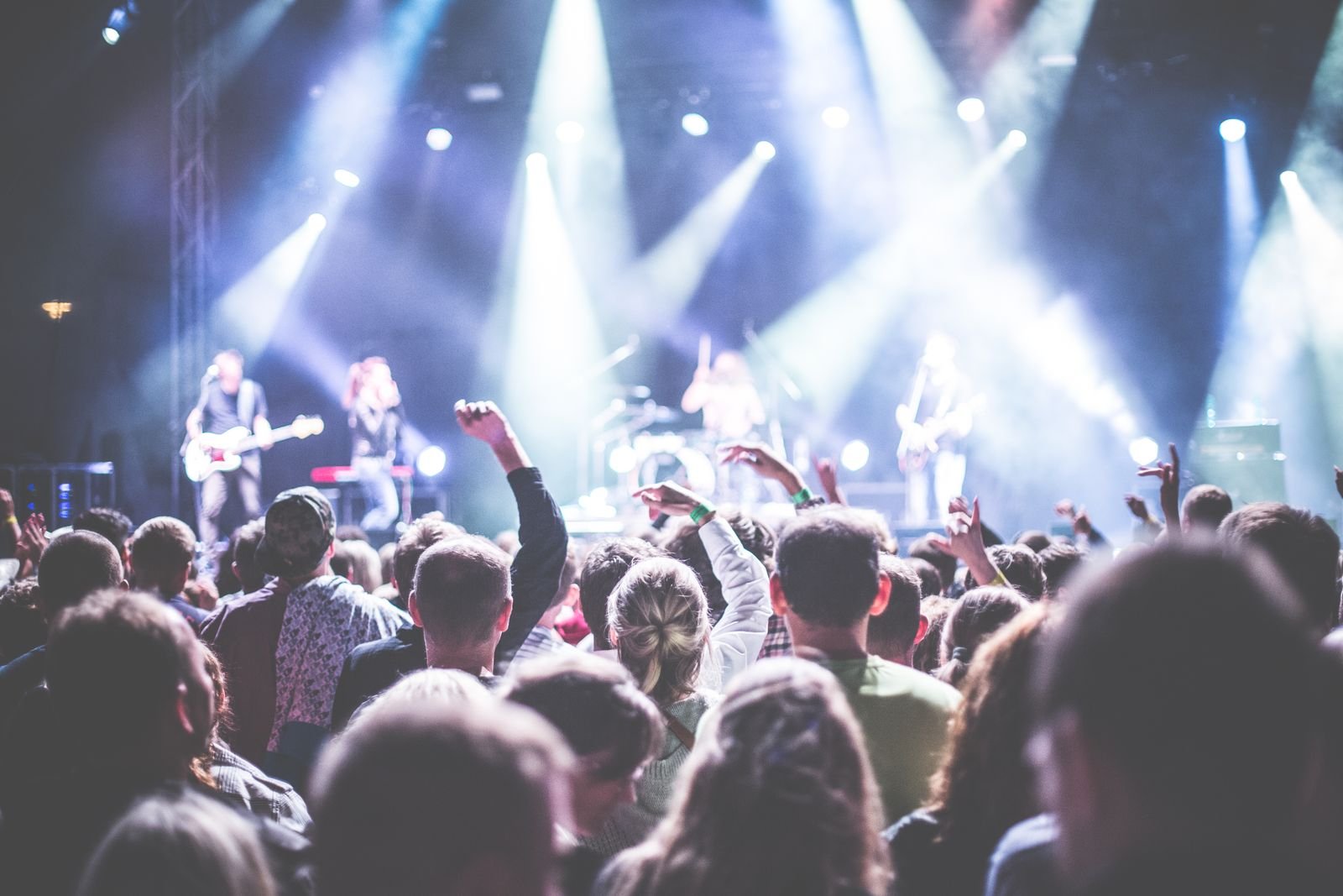 Packed concert crowd with hands raised under blue stage lights