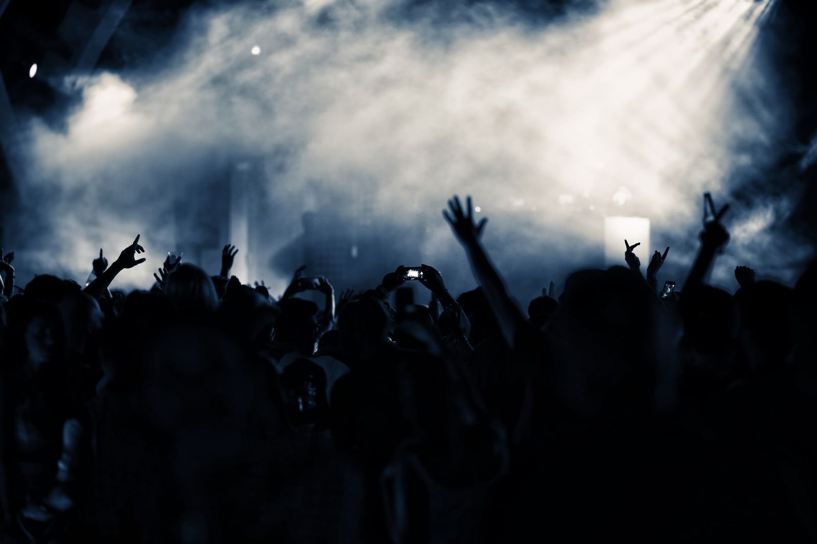 A concert crowd at night lit in warm tones, hands raised
