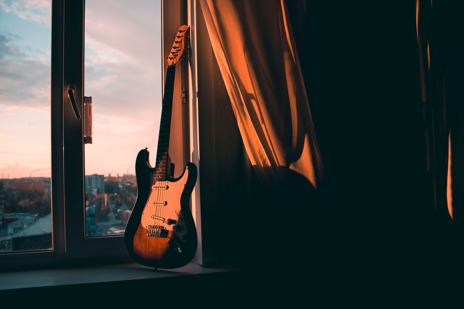 A sunburst Stratocaster resting on a windowsill at sunset, moody light