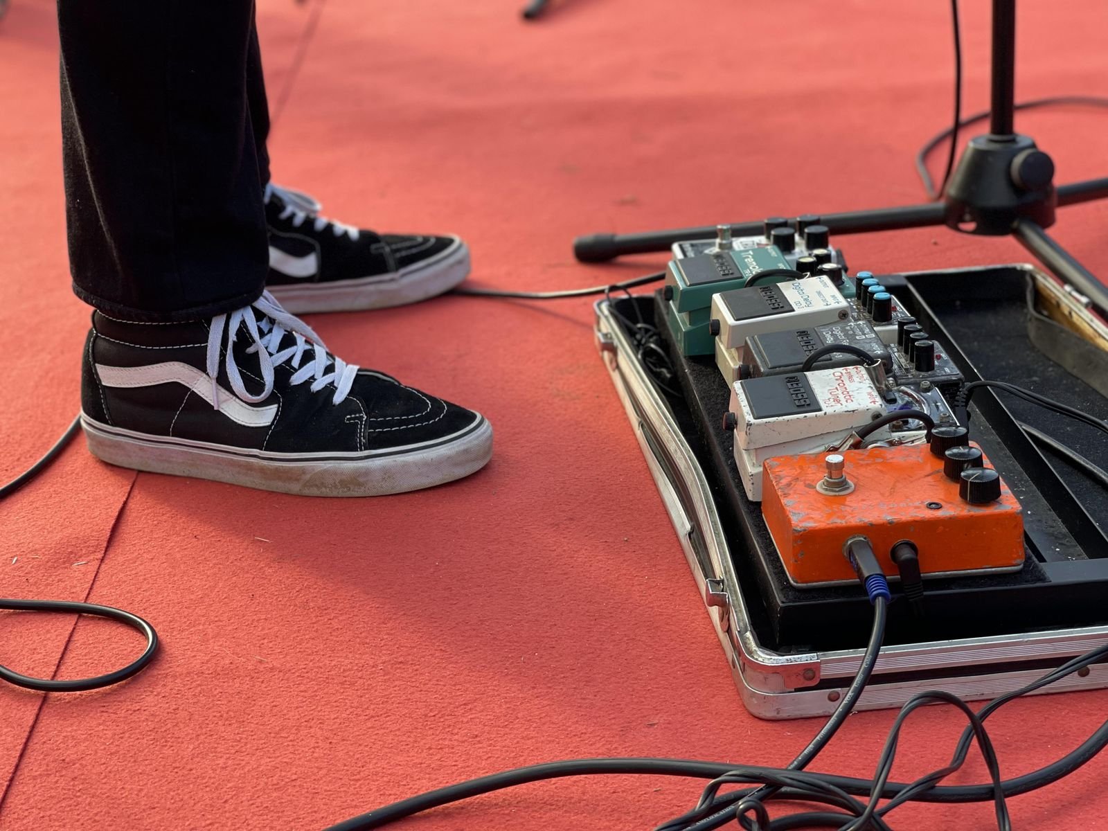 Guitar pedals and a pedalboard laid out on a red stage floor next to a pair of sneakers