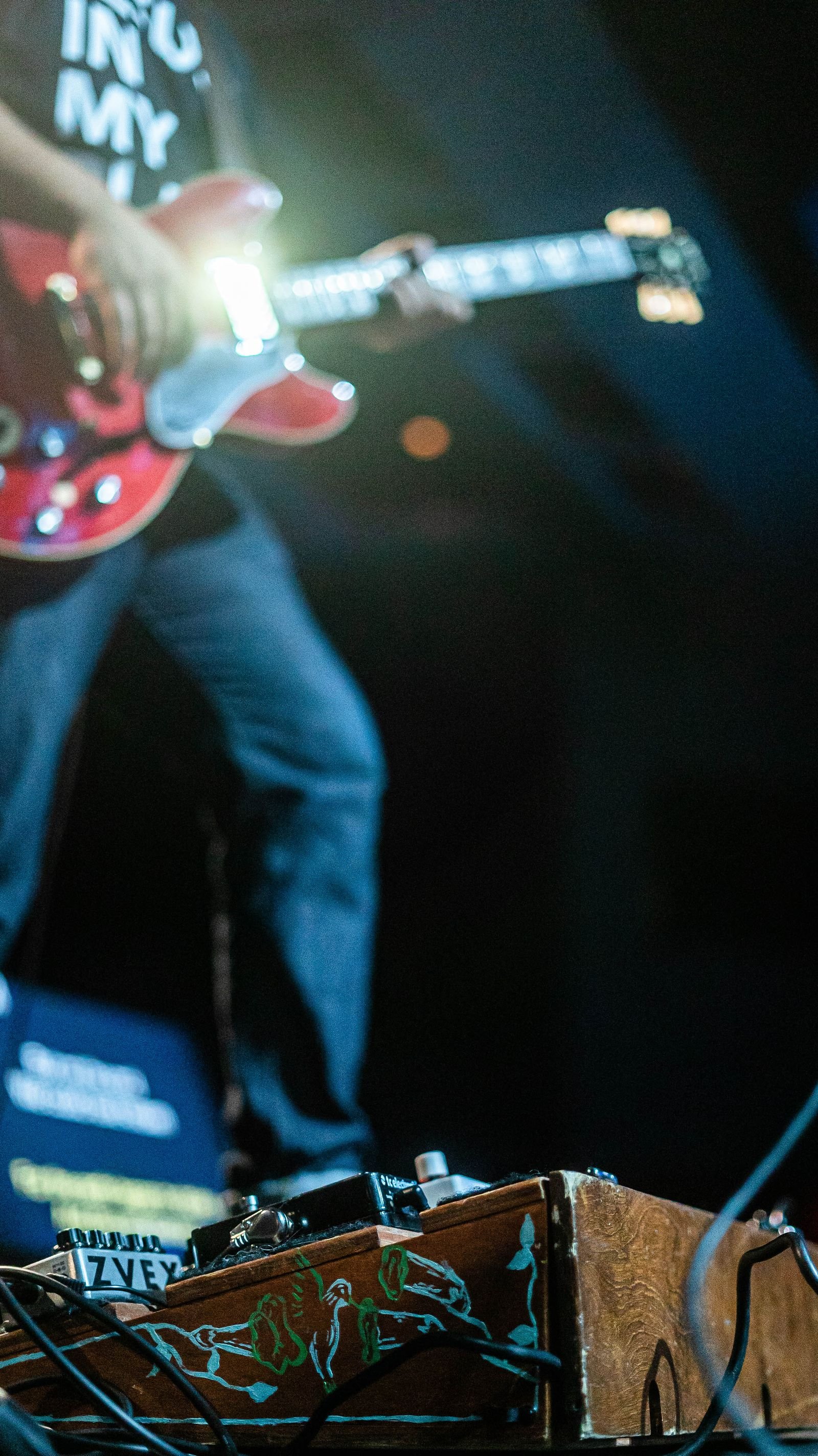 A single fuzz effect pedal sitting on a stage floor under colored light