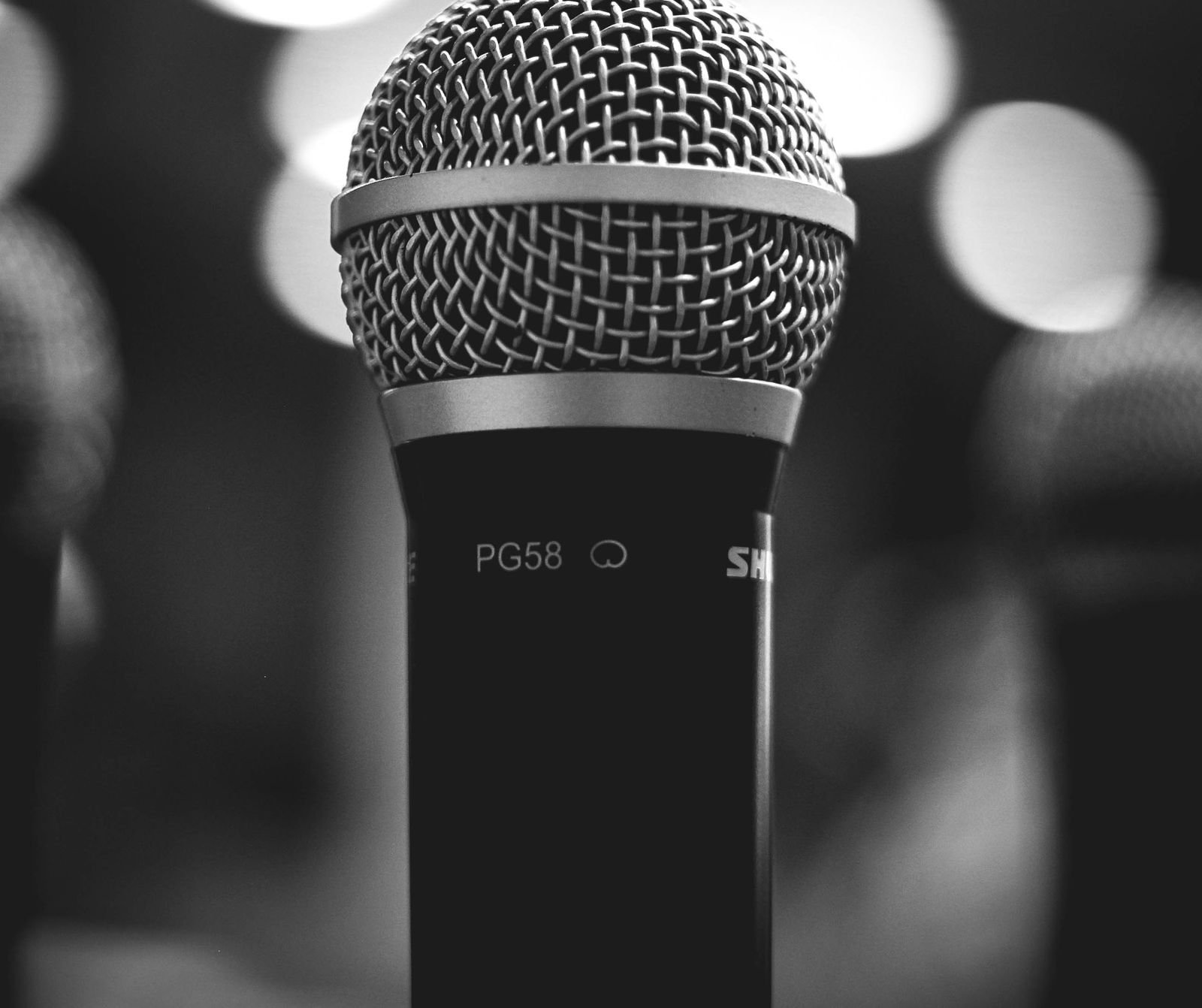 A black-and-white close-up of a Shure microphone, intimate and detailed